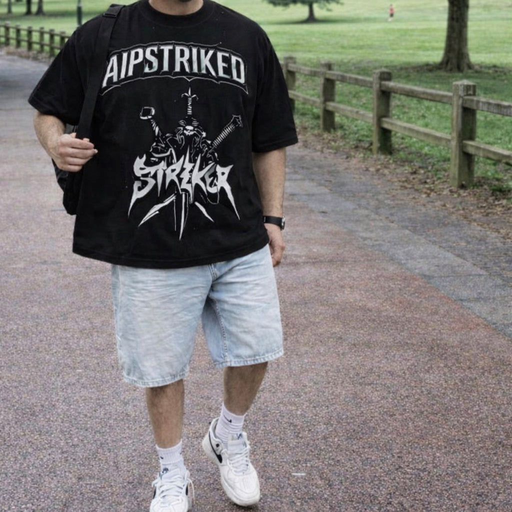 Person wearing a black t-shirt with 'AIPSTRIKED' design in a park setting