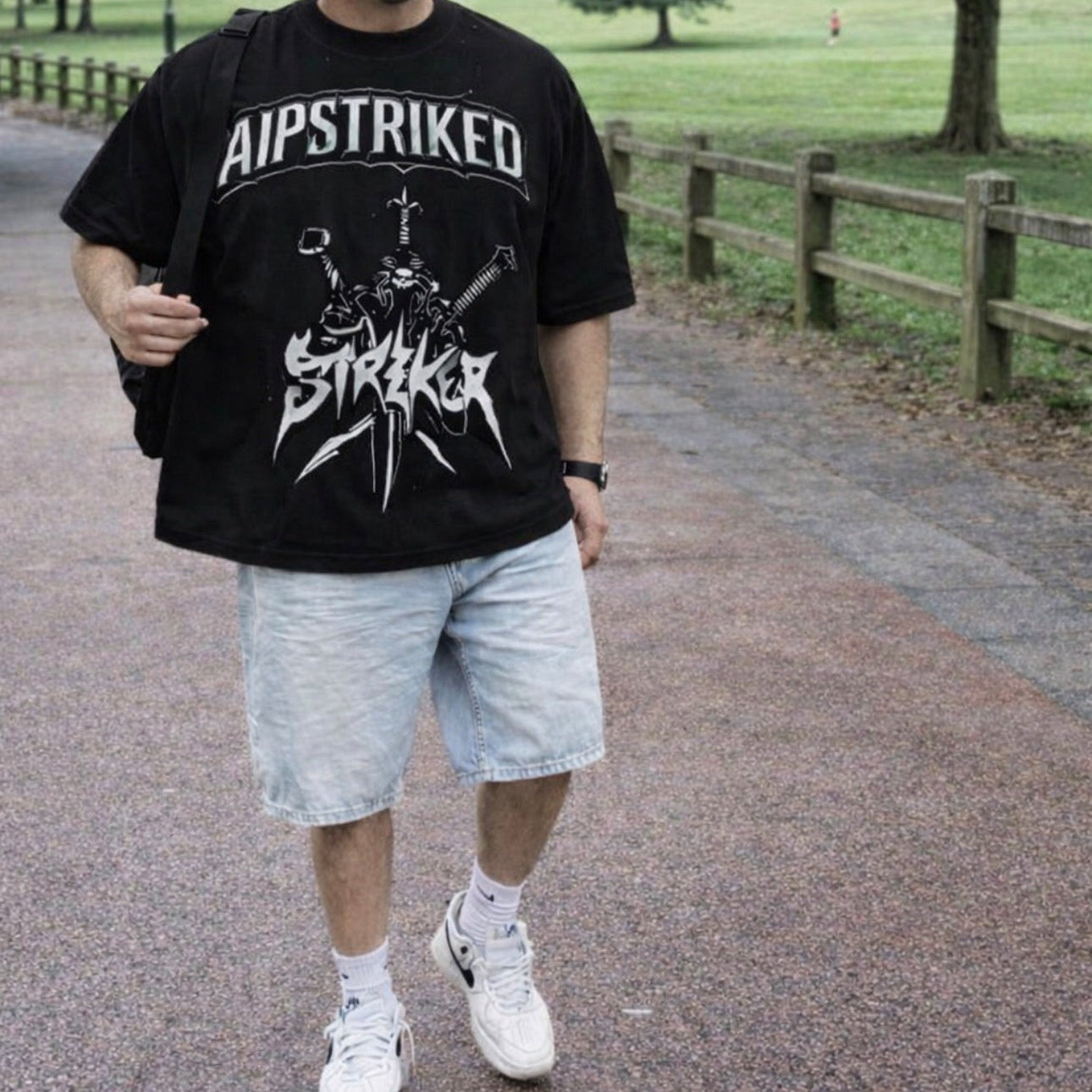 Person wearing a black t-shirt with 'AIPSTRIKED' design in a park setting