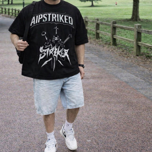 Person wearing a black t-shirt with 'AIPSTRIKED' design in a park setting